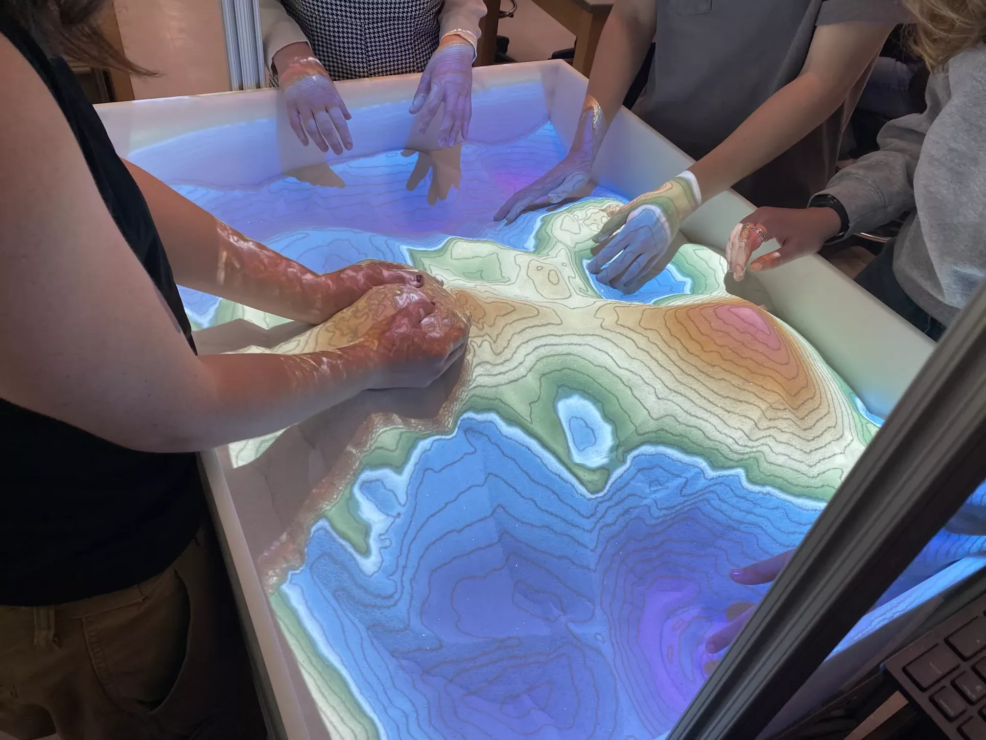 An up close view of students using the digital sandbox, moving the sand around and changing the digital map projected on top of the sand